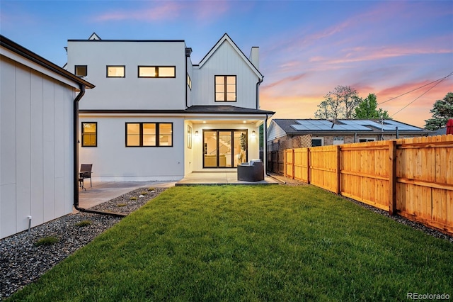 back house at dusk featuring a yard and a patio