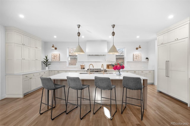 kitchen with white cabinetry, an island with sink, decorative backsplash, a breakfast bar, and light wood-type flooring