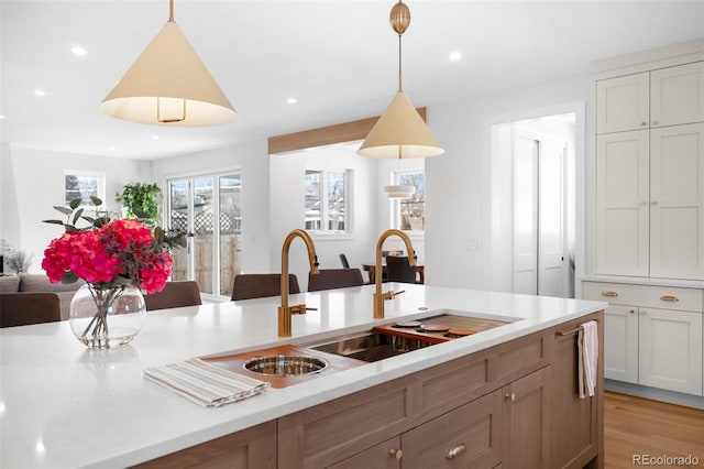 kitchen with pendant lighting, white cabinetry, sink, and light hardwood / wood-style flooring