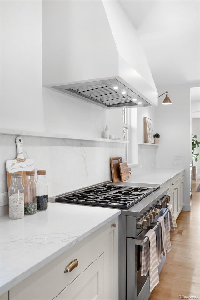 kitchen featuring lofted ceiling, ventilation hood, white cabinets, range with two ovens, and light stone countertops