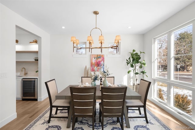 dining space with wood-type flooring, an inviting chandelier, wine cooler, and sink