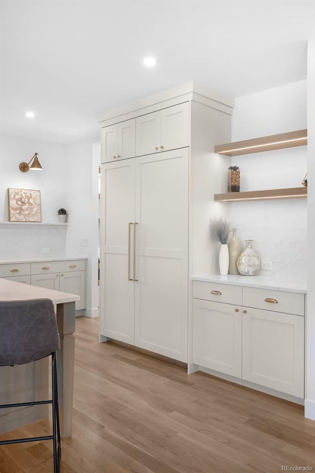 kitchen with a kitchen bar, decorative backsplash, white cabinetry, and light hardwood / wood-style flooring