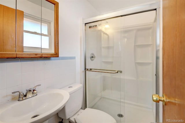 bathroom featuring a shower with door, backsplash, sink, toilet, and tile walls