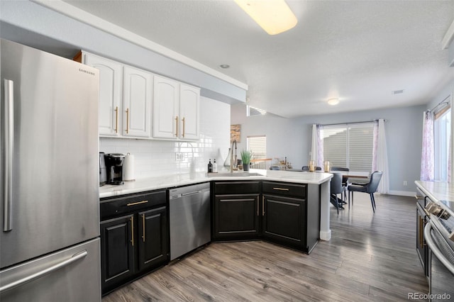 kitchen featuring white cabinetry, appliances with stainless steel finishes, kitchen peninsula, light hardwood / wood-style flooring, and tasteful backsplash