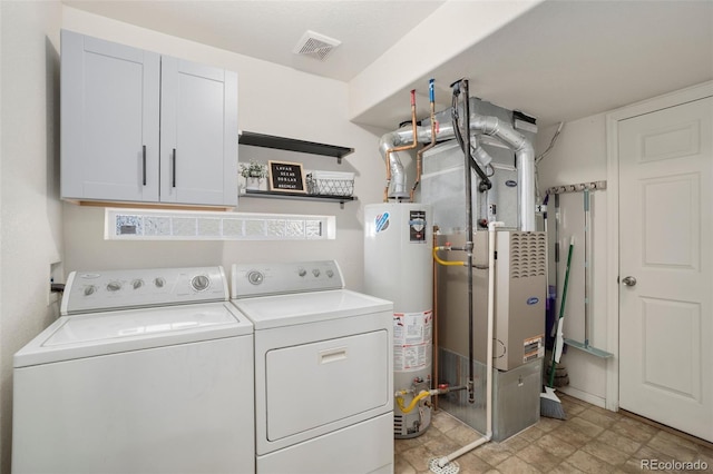 clothes washing area featuring gas water heater, washer and dryer, and cabinets