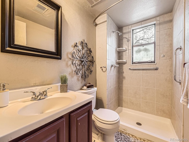 bathroom featuring a textured ceiling, toilet, vanity, and a tile shower