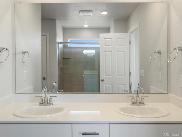 bathroom with a sink, a textured ceiling, a stall shower, and double vanity