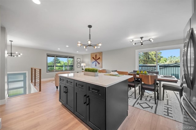 kitchen with a chandelier, freestanding refrigerator, dark cabinetry, a center island, and decorative light fixtures