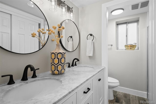 bathroom featuring wood finished floors, toilet, double vanity, and baseboards