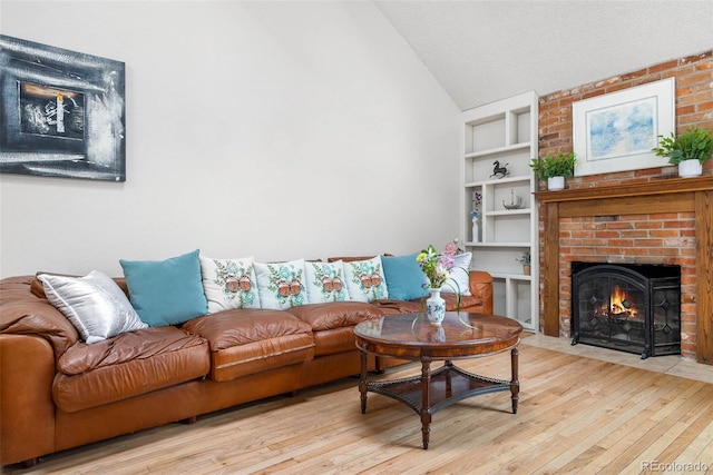 living room with built in features, a fireplace, a textured ceiling, vaulted ceiling, and light wood-type flooring