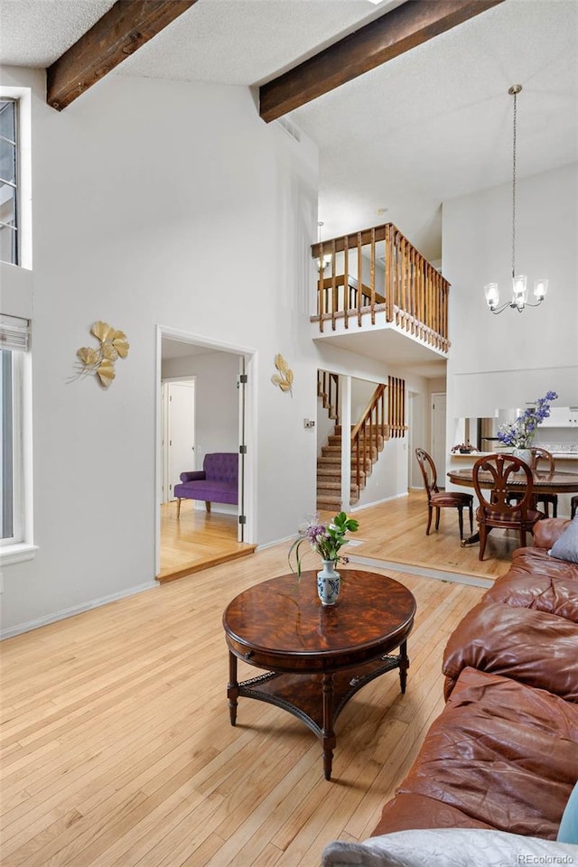 living room featuring beamed ceiling, wood-type flooring, a notable chandelier, and a textured ceiling