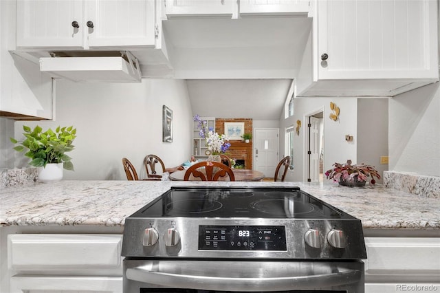 kitchen with electric stove, light stone counters, white cabinetry, and vaulted ceiling