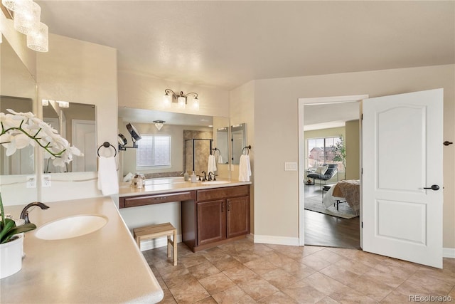 bathroom with double vanity, a shower with door, baseboards, and a sink