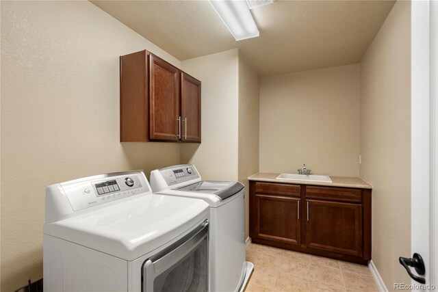 laundry area with a sink, cabinet space, light tile patterned floors, baseboards, and washing machine and clothes dryer