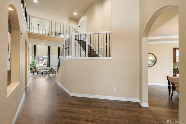 corridor with wood finished floors, stairway, arched walkways, baseboards, and a towering ceiling