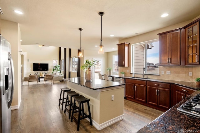 kitchen with a center island, decorative backsplash, appliances with stainless steel finishes, wood finished floors, and a sink