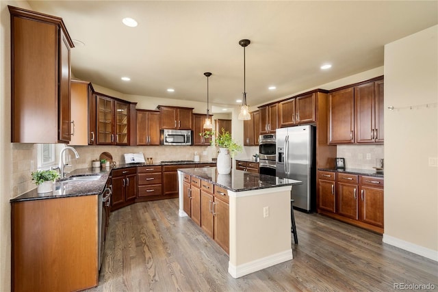 kitchen featuring a kitchen island, dark wood finished floors, a sink, stainless steel appliances, and glass insert cabinets