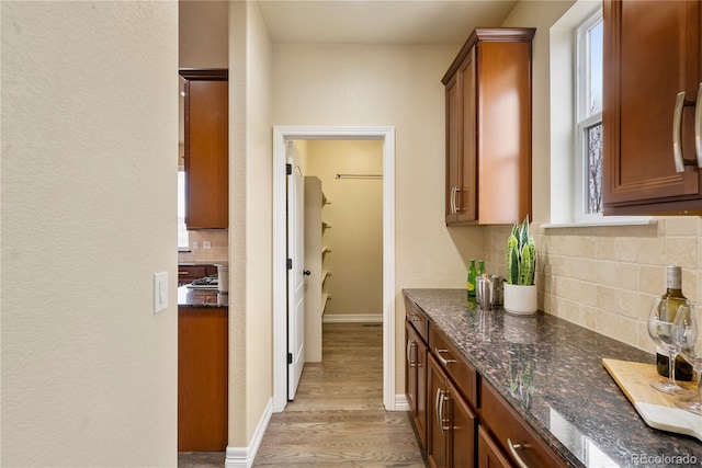 kitchen with brown cabinetry, baseboards, dark stone counters, light wood-style flooring, and tasteful backsplash