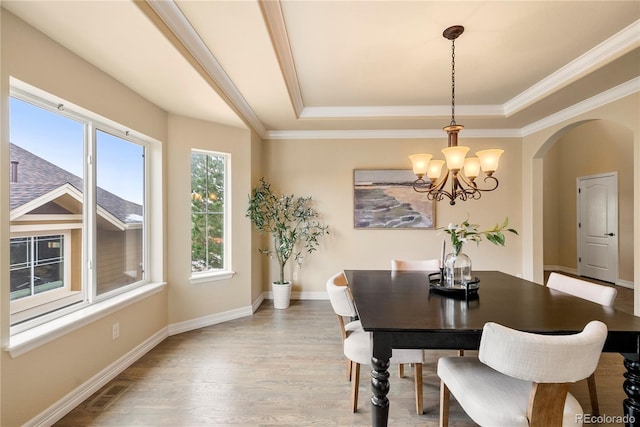 dining room featuring visible vents, light wood-style flooring, a tray ceiling, arched walkways, and baseboards