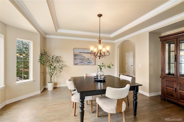 dining space with a raised ceiling, wood finished floors, arched walkways, and baseboards