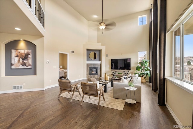 living room with a tiled fireplace, dark wood-type flooring, visible vents, and a wealth of natural light