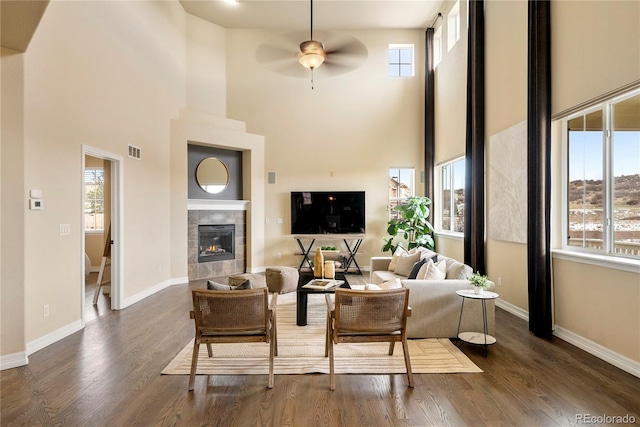 living area featuring dark wood-style floors, a tile fireplace, a ceiling fan, and baseboards