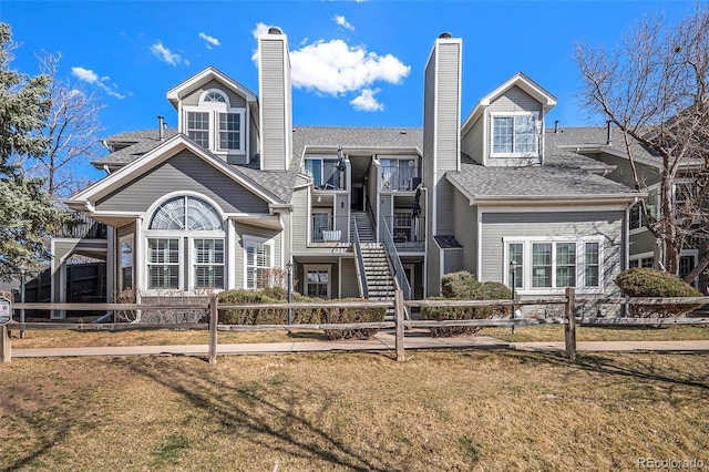 view of front of property with a fenced front yard, a shingled roof, stairs, and a front yard