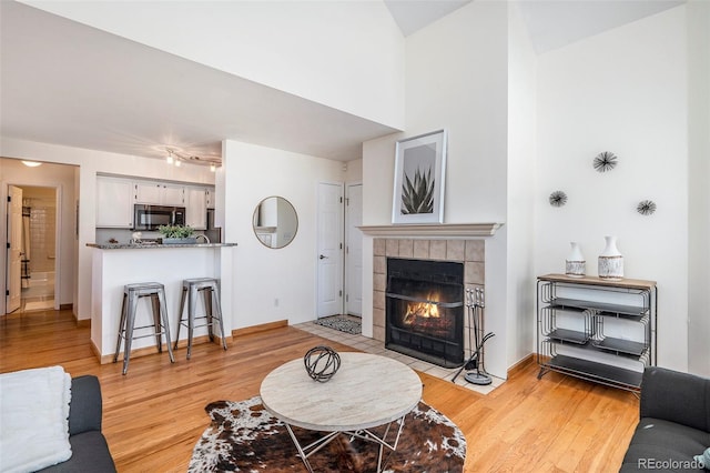 living area featuring light wood-type flooring, baseboards, and a tile fireplace