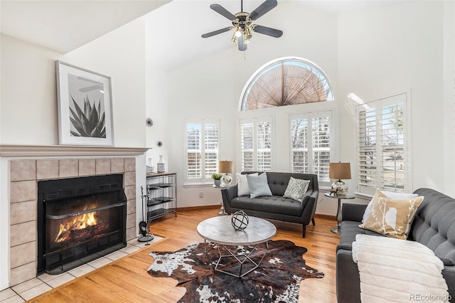 living area featuring light wood-style flooring, a fireplace, high vaulted ceiling, and baseboards