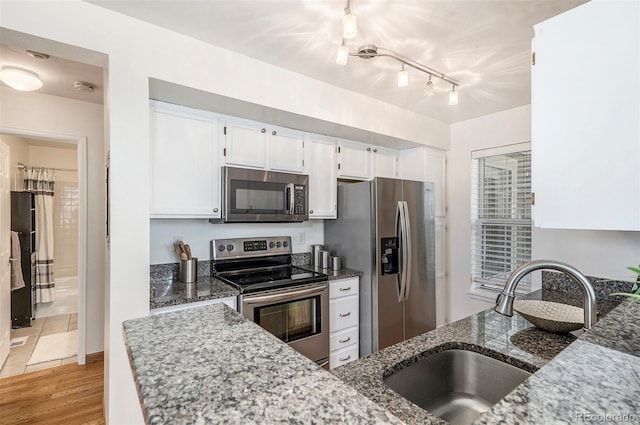 kitchen with dark stone countertops, light wood-style flooring, stainless steel appliances, white cabinetry, and a sink