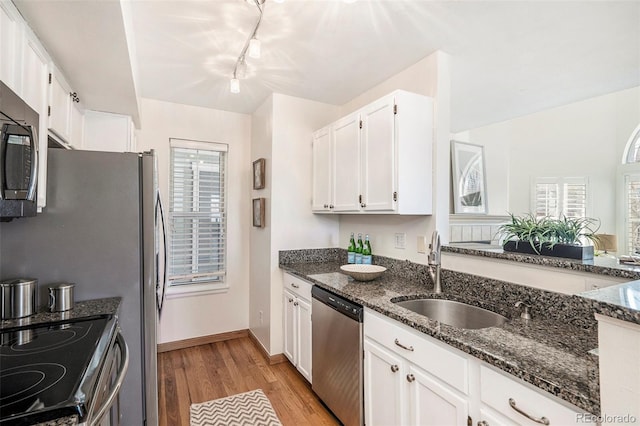 kitchen with a sink, dark stone countertops, appliances with stainless steel finishes, white cabinets, and light wood finished floors