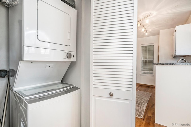 laundry room featuring track lighting, laundry area, stacked washing maching and dryer, wood finished floors, and a sink