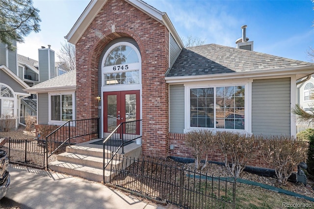 view of front facade featuring brick siding, french doors, and fence