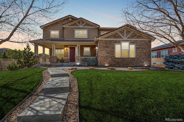 craftsman-style home with covered porch, stone siding, a front lawn, and stucco siding