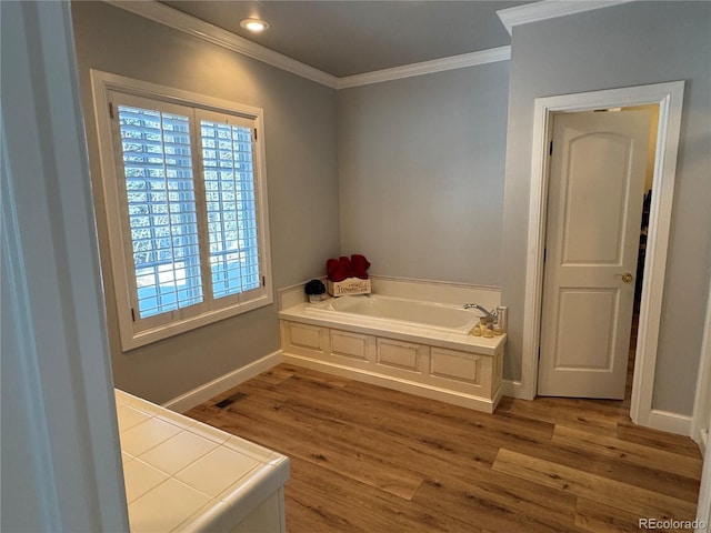 bathroom featuring hardwood / wood-style flooring, ornamental molding, and a bathing tub