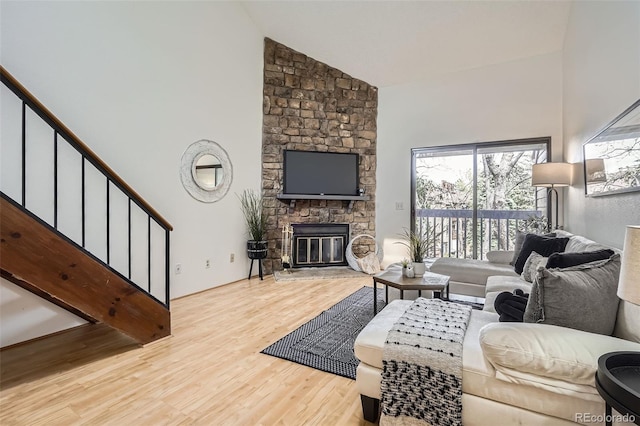 living room featuring high vaulted ceiling, wood finished floors, a stone fireplace, and stairs