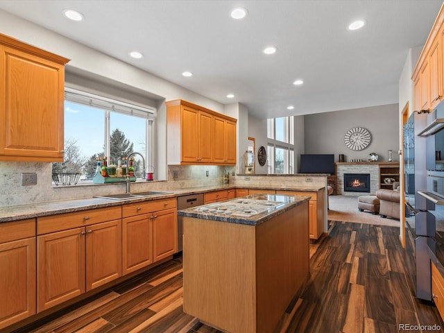 kitchen featuring open floor plan, a kitchen island, a sink, light stone countertops, and a peninsula