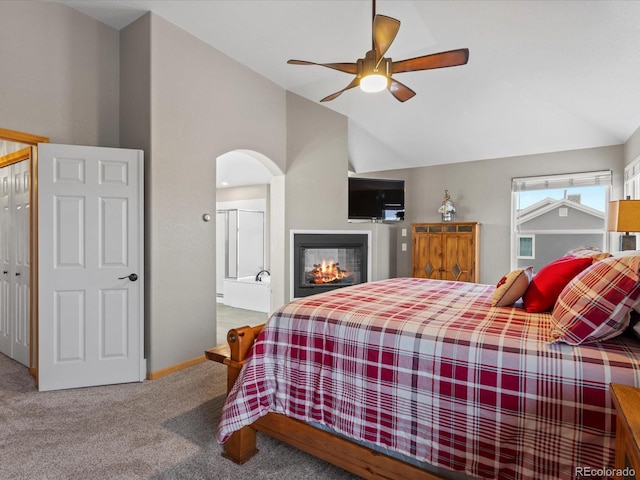 bedroom featuring light carpet, arched walkways, a glass covered fireplace, ceiling fan, and vaulted ceiling