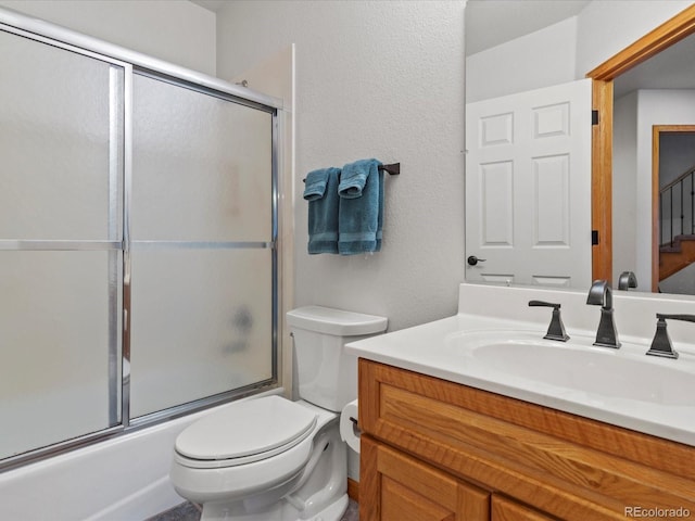 bathroom with toilet, shower / bath combination with glass door, a textured wall, and vanity