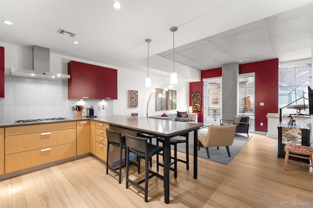 kitchen featuring light hardwood / wood-style flooring, gas cooktop, backsplash, decorative light fixtures, and wall chimney exhaust hood