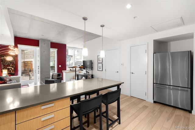 kitchen featuring stainless steel fridge, light hardwood / wood-style floors, and hanging light fixtures