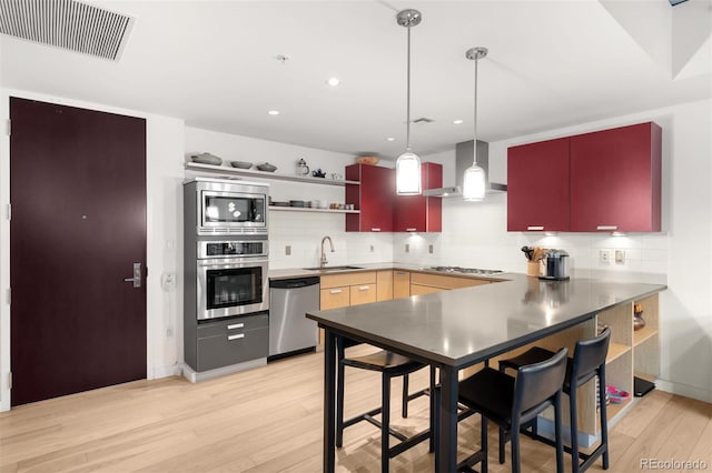 kitchen with appliances with stainless steel finishes, tasteful backsplash, sink, light hardwood / wood-style floors, and wall chimney exhaust hood