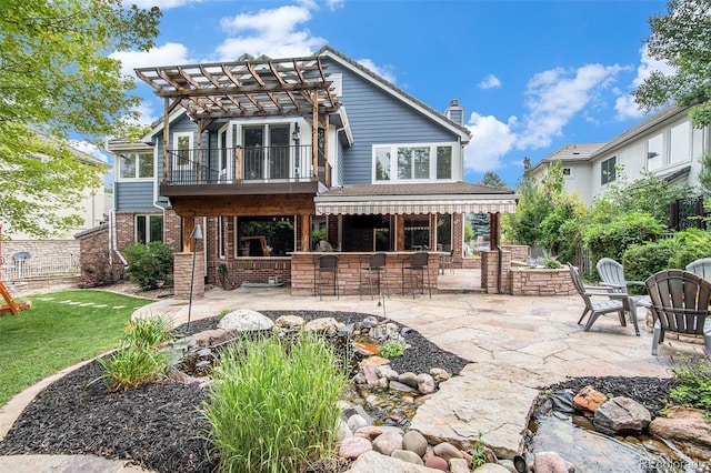 rear view of property featuring brick siding, outdoor dry bar, a chimney, a patio area, and a pergola