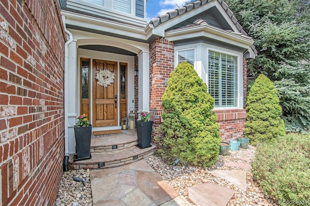 view of exterior entry with brick siding and a tiled roof