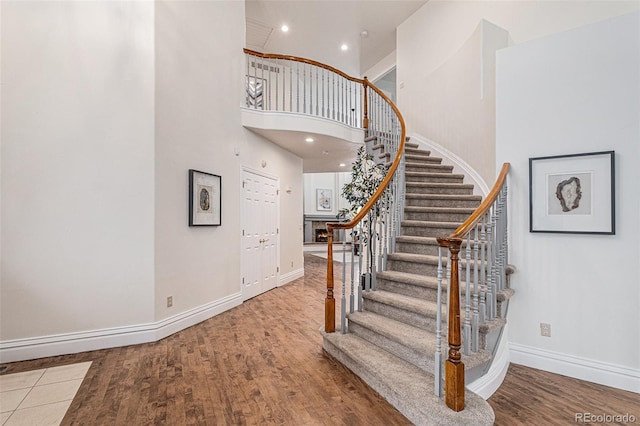 stairs with a towering ceiling, recessed lighting, baseboards, and wood finished floors