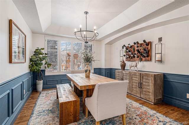 dining area with light wood-style floors, a tray ceiling, a textured ceiling, and a wainscoted wall