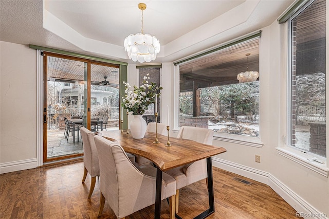 dining room featuring an inviting chandelier, wood finished floors, baseboards, and a tray ceiling