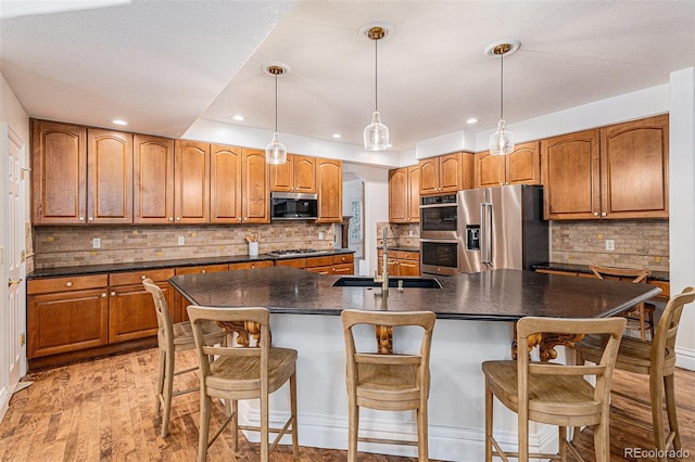 kitchen featuring a sink, dark countertops, stainless steel appliances, light wood-style floors, and brown cabinetry