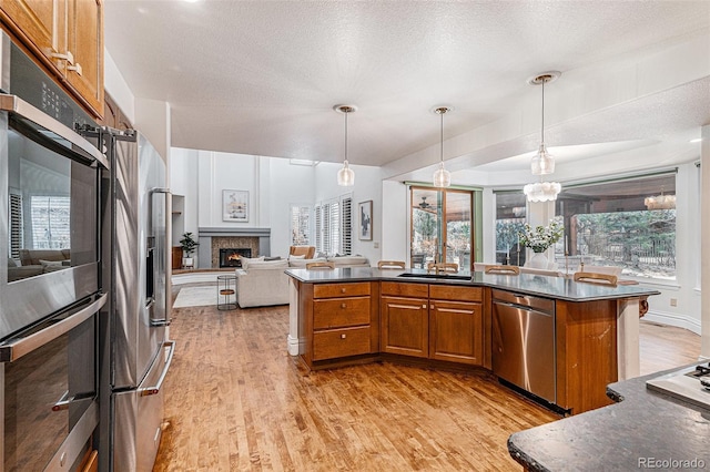 kitchen featuring stainless steel appliances, brown cabinets, dark countertops, and a warm lit fireplace