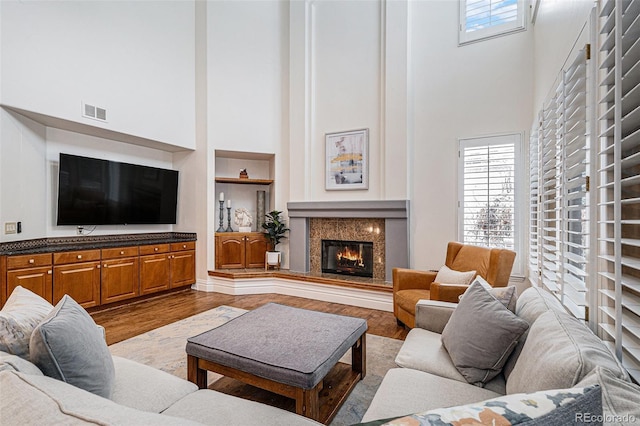 living area featuring built in features, wood finished floors, visible vents, a high end fireplace, and a towering ceiling